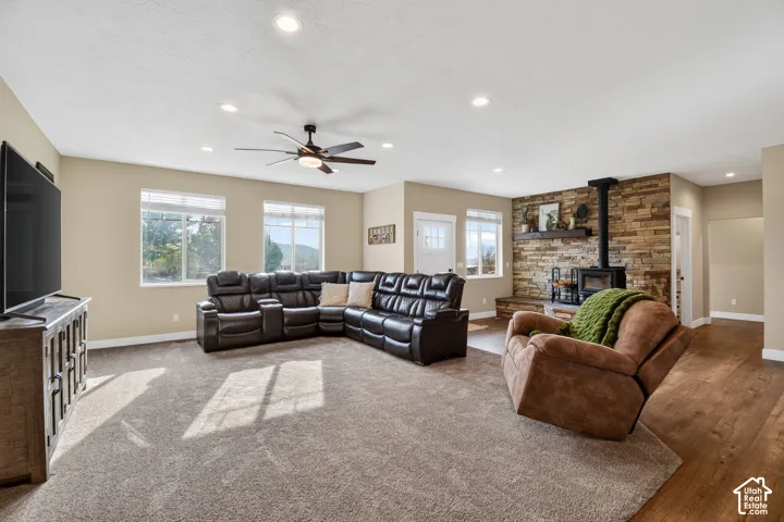 Spacious living area featuring a stone accent wall with a wood-burning stove, multiple windows, recessed lighting, and a ceiling fan
