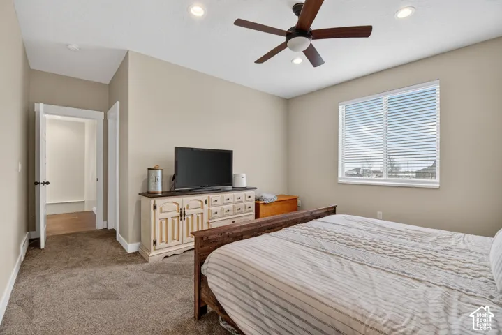 Carpeted bedroom featuring a ceiling fan with integrated lighting, recessed ceiling lights, a window with horizontal blinds, and a doorway opening to a wood-finish floor