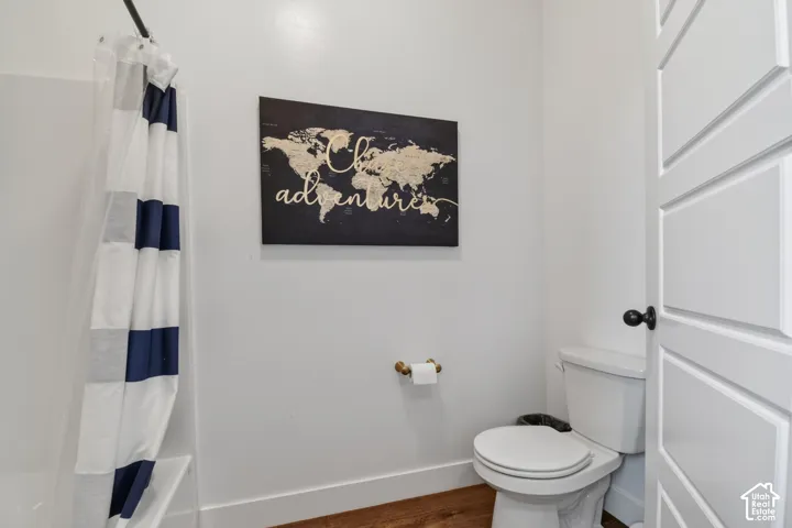 Bathroom featuring white walls, wood-finish flooring, and a shower with a privacy curtain