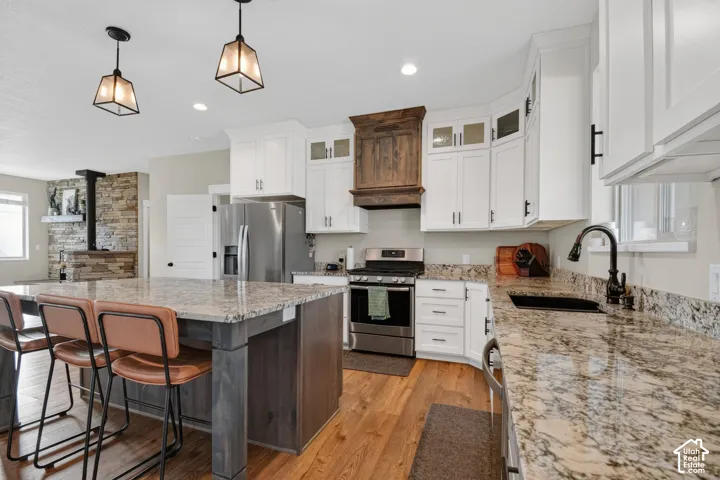 Kitchen featuring white cabinetry, granite countertops, stainless steel appliances, a large island with seating, and wood-finish flooring
