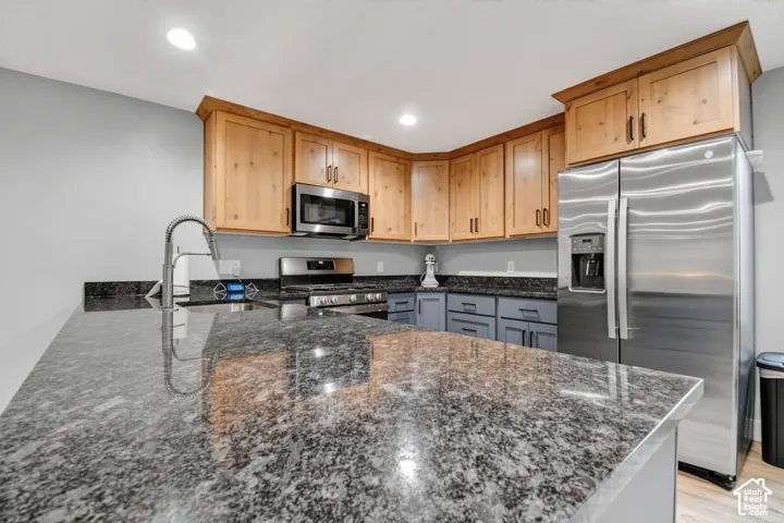 Kitchen featuring extensive stone countertops, stainless steel appliances, light wood-finish upper cabinetry, and contrasting lower cabinetry