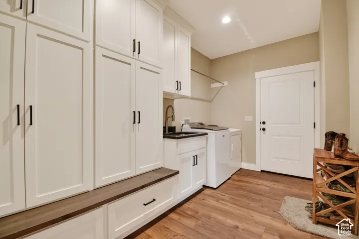 Mudroom featuring extensive white cabinetry, a built-in bench with a wood-finish top, wood-finish flooring, a utility sink with a dark countertop, and a white door with dark hardware