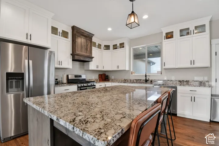Kitchen featuring a large central island with a stone countertop, white cabinetry with display accents, stainless steel appliances, and wood-finish flooring