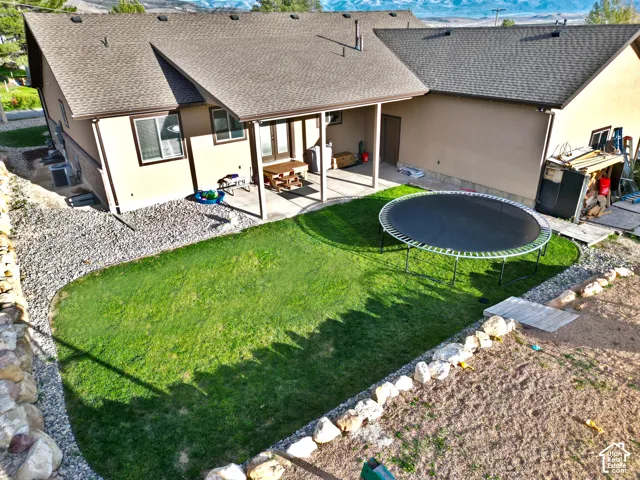 Expansive backyard featuring a manicured lawn, covered patio, gravel landscaping, and a partial retaining wall