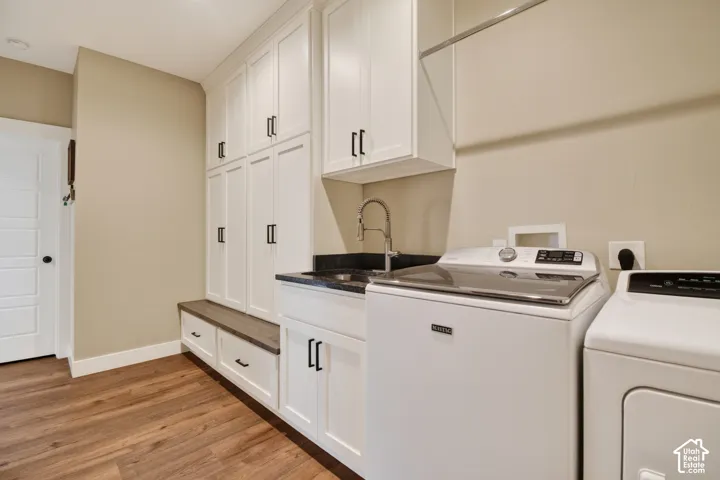 Laundry area featuring wood-finish flooring, white cabinetry with dark hardware, a built-in bench with storage, a dark countertop with an integrated sink, and a wall-mounted drying rod