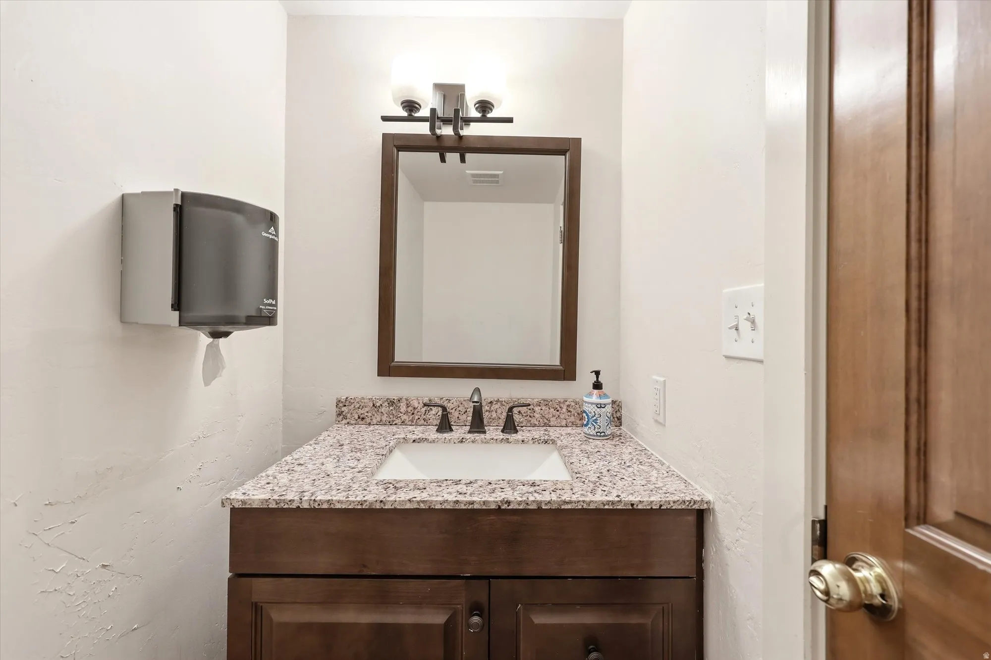 Powder room featuring a dark wood-finish vanity with a granite-style countertop and an undermount sink