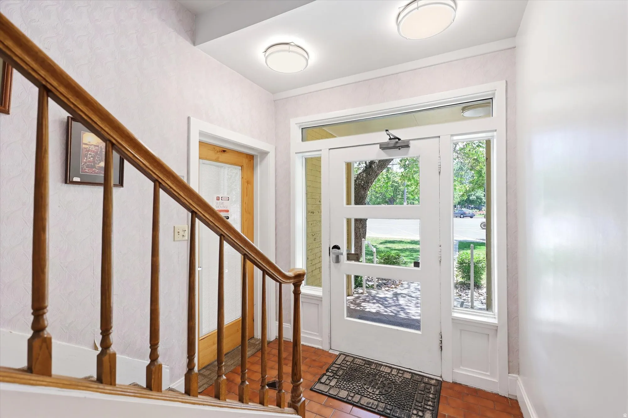 Entry area featuring a wood-finish staircase with balusters, a multi-pane glass-insert entry door with sidelights and transom, two flush-mount ceiling lights, and patterned wallpaper