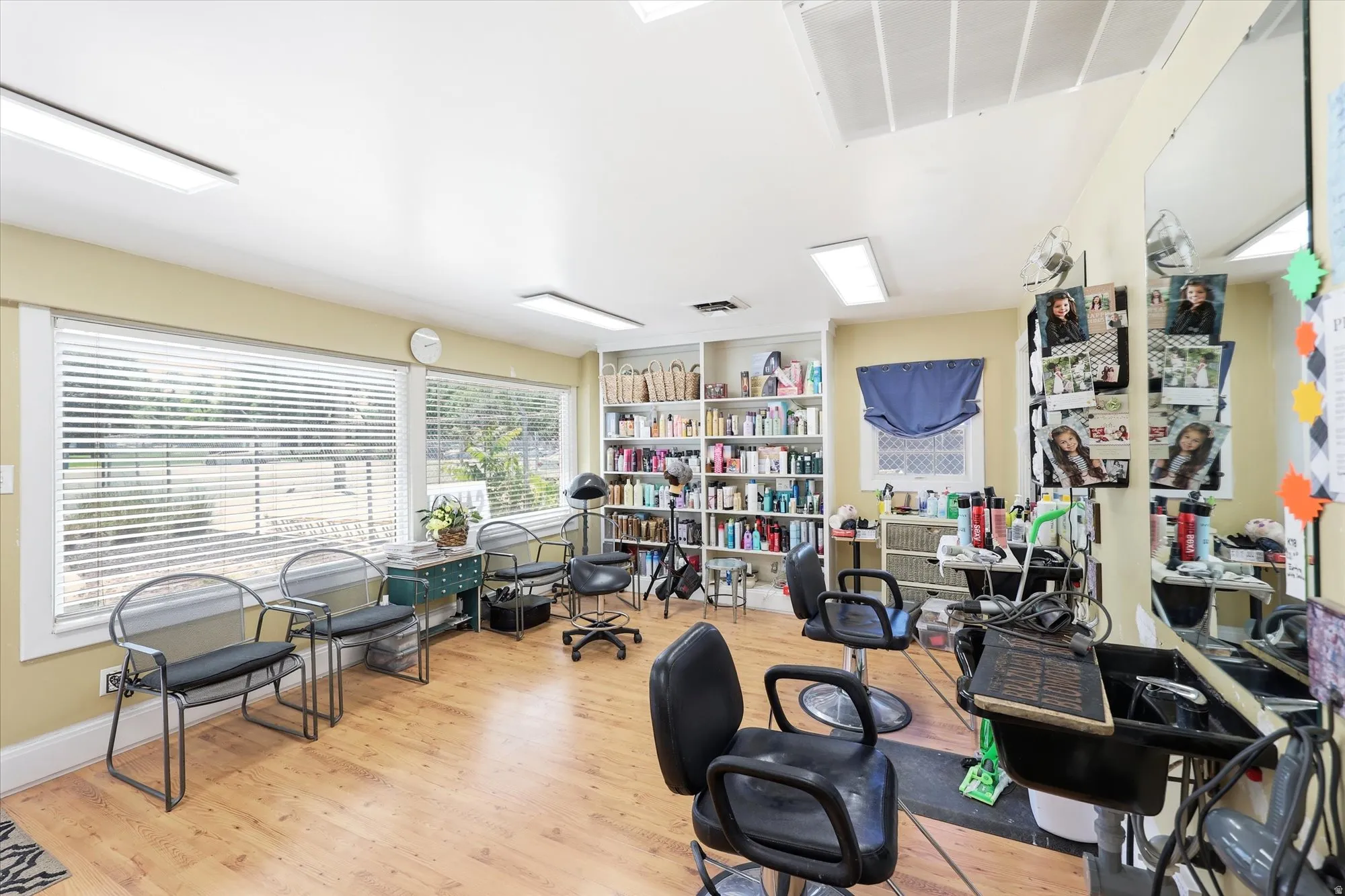 Open-concept commercial space featuring wood-finish flooring, multiple windows with horizontal blinds, and extensive built-in shelving