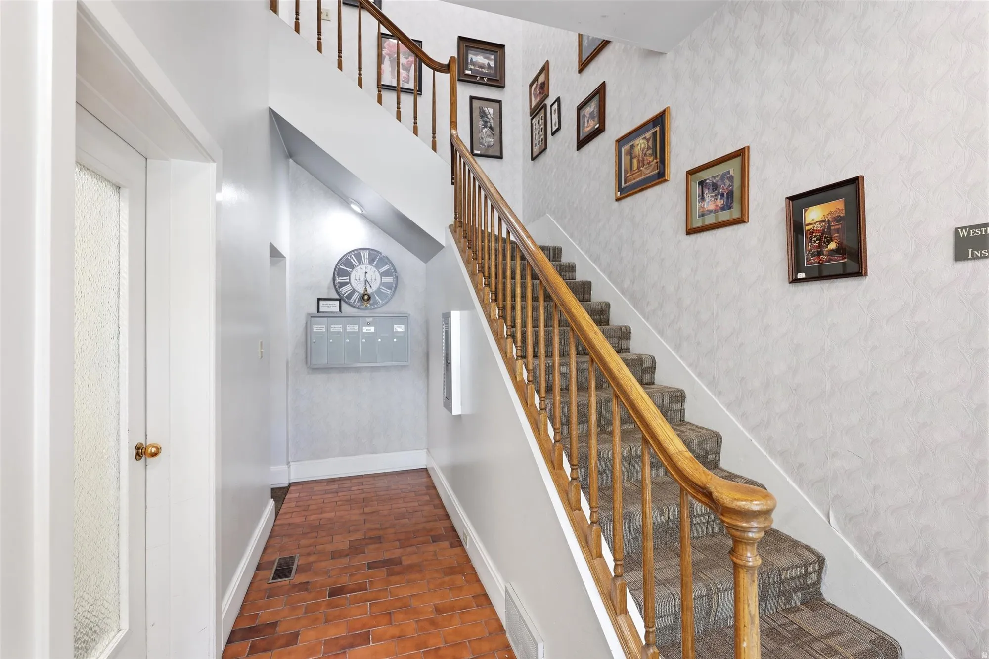 Staircase with wood banister and carpeted treads, complemented by a brick-finish floor in the entryway