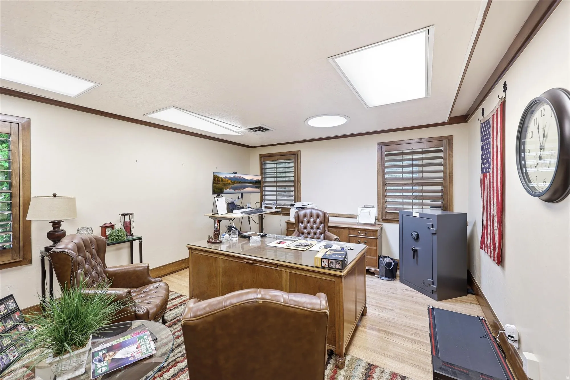 Dedicated office space featuring hardwood flooring, wood trim, two windows with plantation shutters, and recessed lighting with a circular skylight