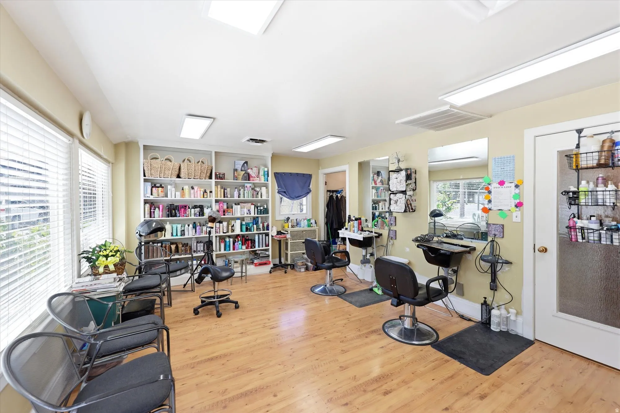 Open-concept commercial space featuring wood-finish flooring, multiple windows with blinds, recessed lighting, and built-in shelving