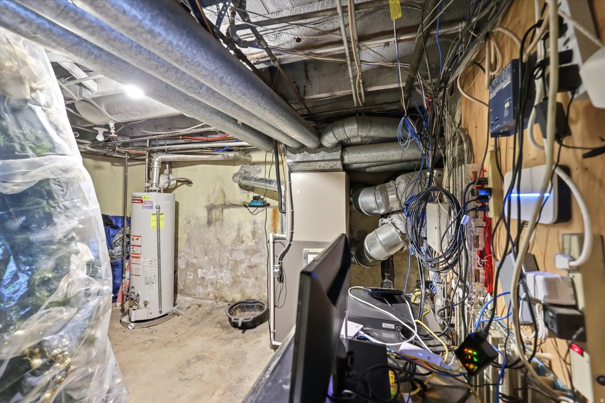 Basement utility area featuring a water heater, exposed ductwork, and overhead piping