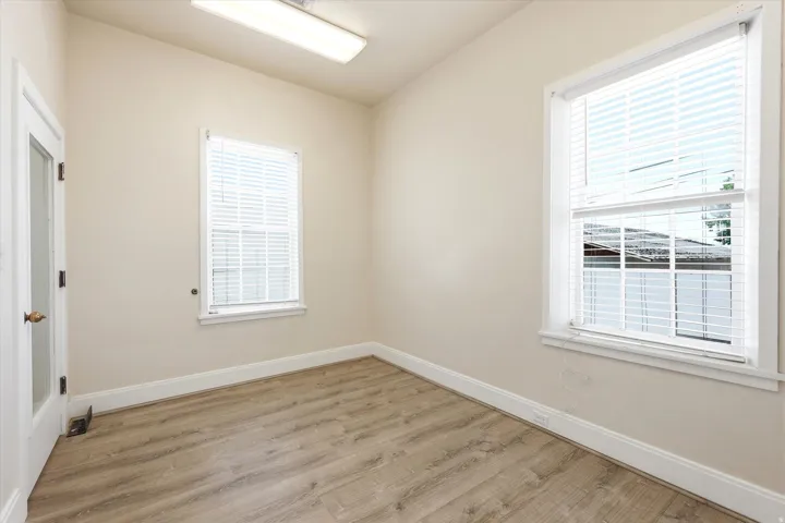 Room featuring two windows with white blinds, wood-finish flooring, light neutral-toned walls, and a glass-paneled door