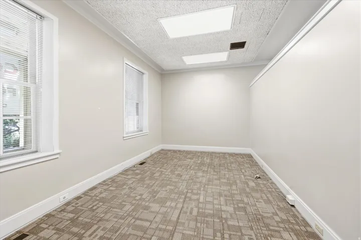 Neutral-toned room featuring two windows with white blinds, textured carpet flooring, white baseboards, and a dropped ceiling with recessed lighting