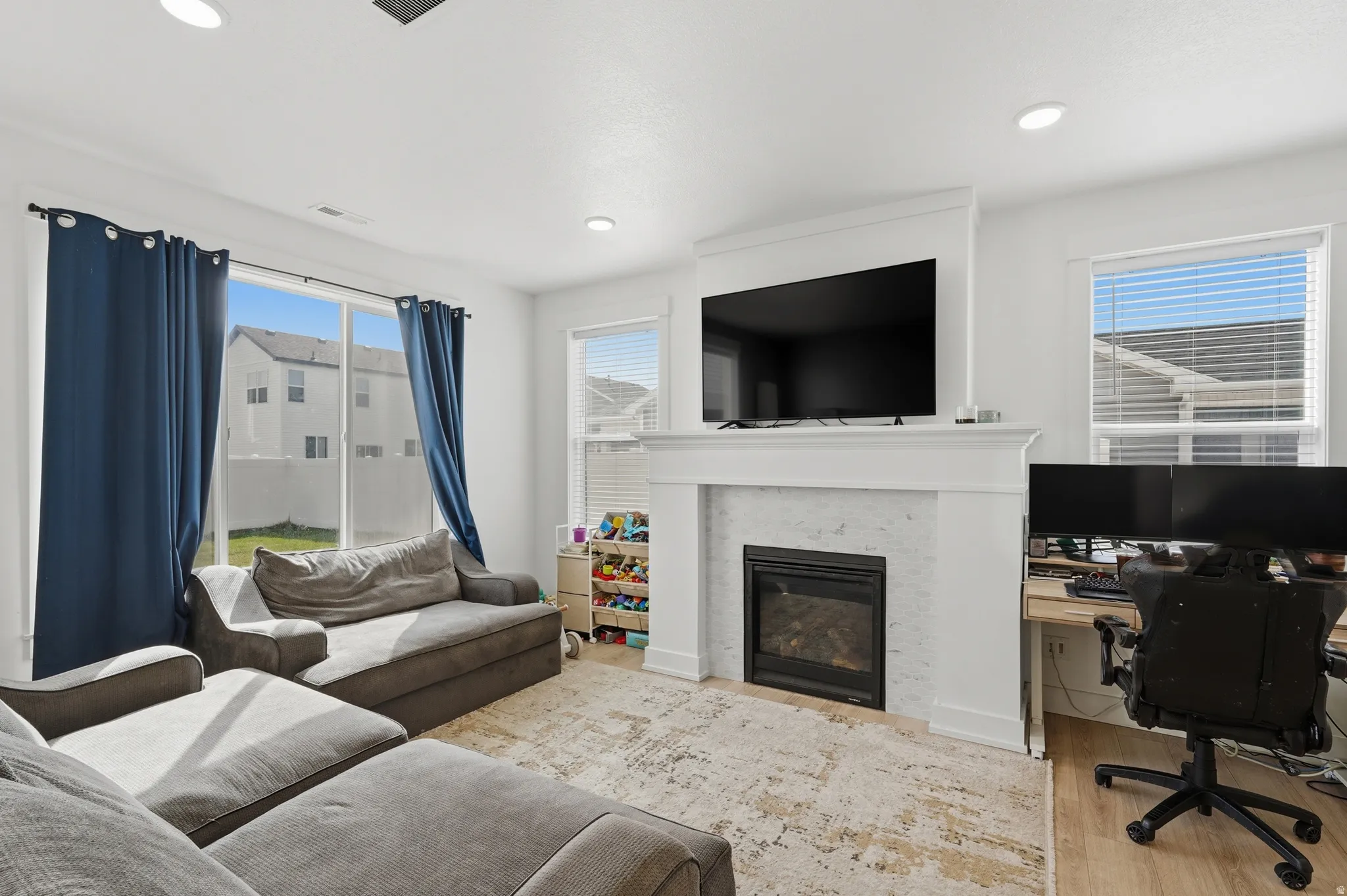 Living area with an office area, a glass covered fireplace, wood finished floors, and recessed lighting
