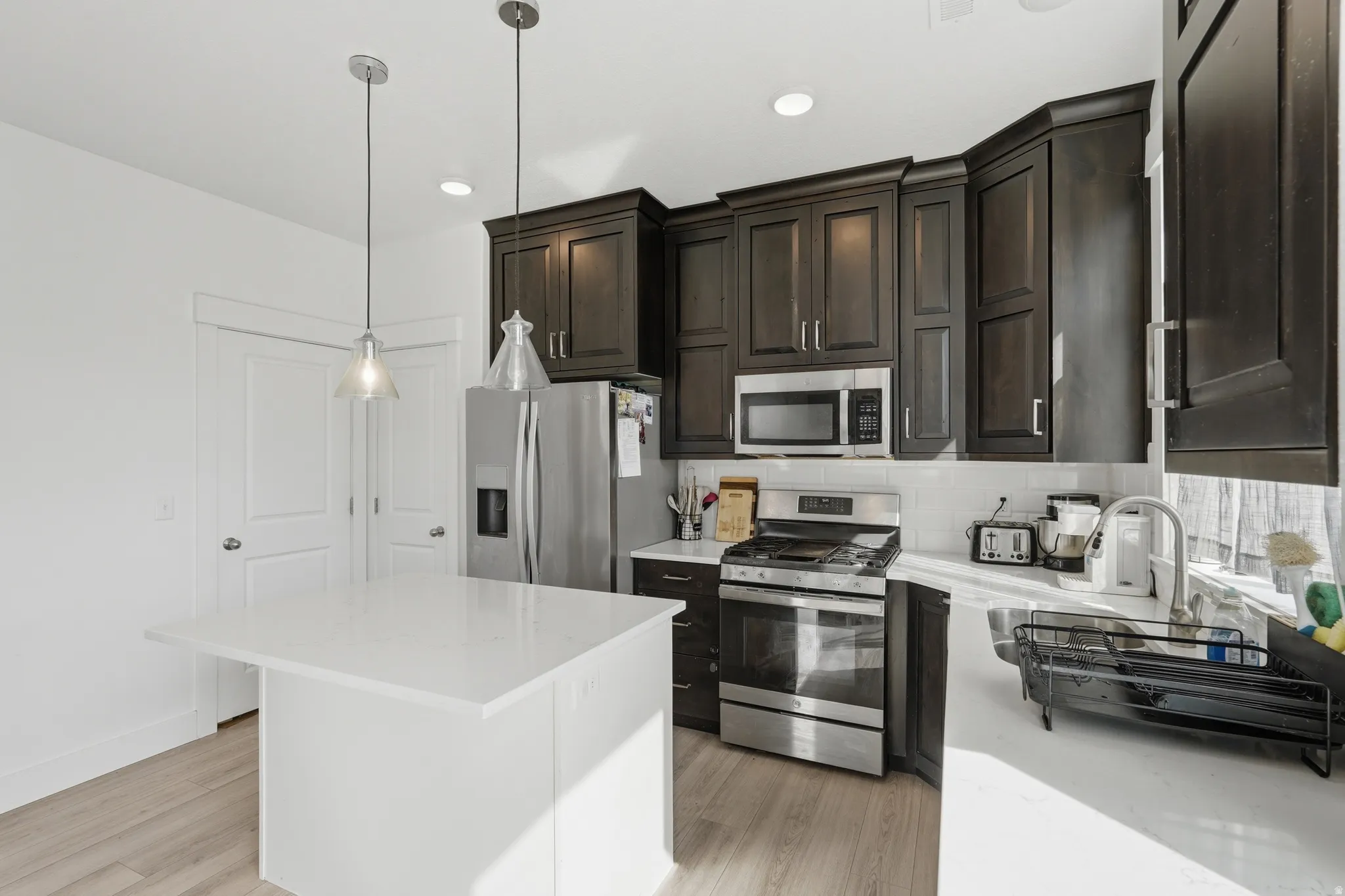 Kitchen with stainless steel appliances, decorative backsplash, dark wood finish cabinets, light wood-style floors, and hanging light fixtures