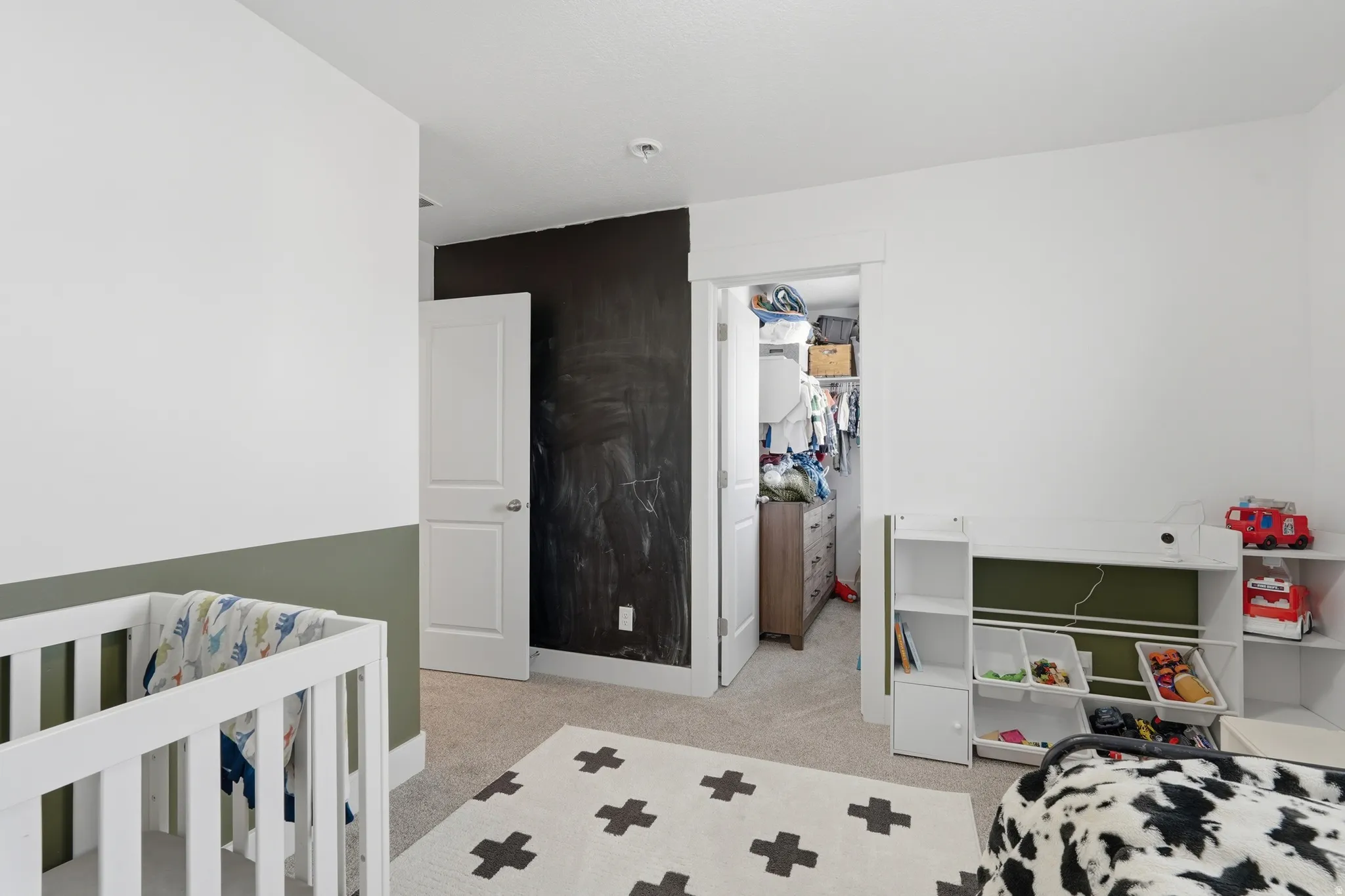 Bedroom featuring light colored carpet, a walk in closet, and a crib