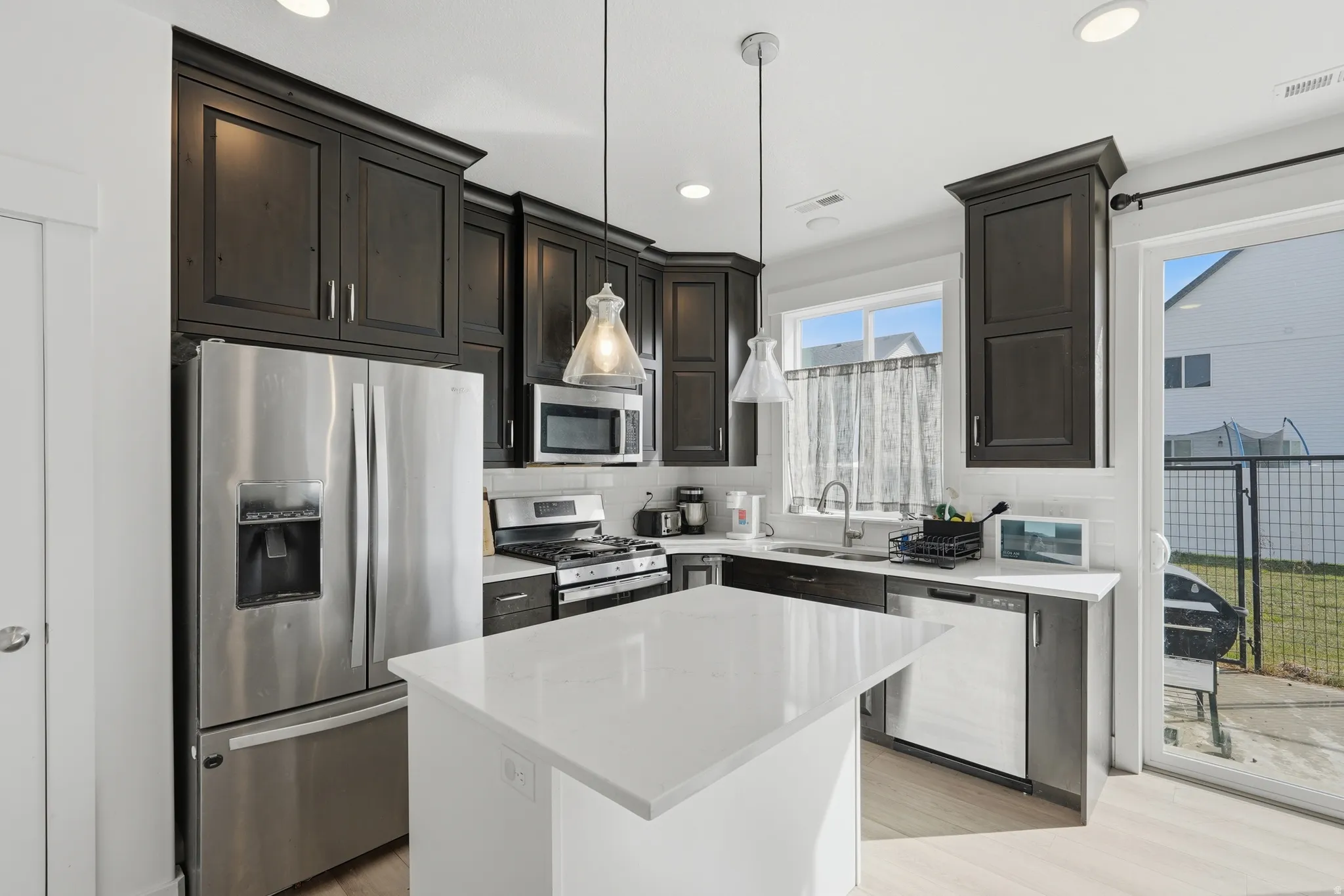 Kitchen featuring stainless steel appliances, light wood-type flooring, a center island, light stone counters, and hanging light fixtures