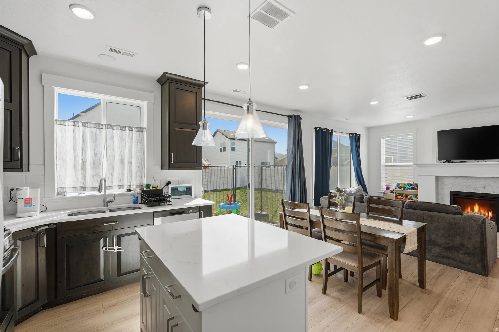 Kitchen with open floor plan, tasteful backsplash, a kitchen island, light wood-style floors, and a warm lit fireplace