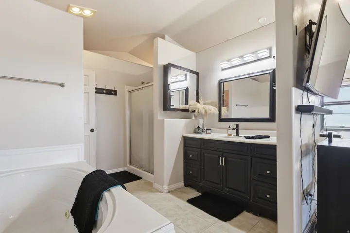 Full bath featuring vanity, a stall shower, a garden tub, light tile patterned flooring, and vaulted ceiling