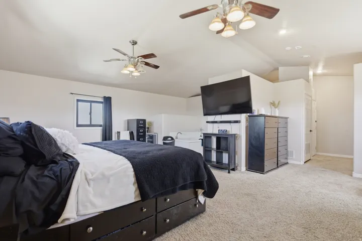 Bedroom with light colored carpet, ceiling fan, and vaulted ceiling