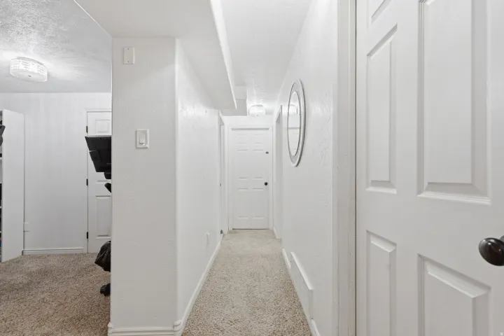 Hall with light colored carpet, a textured wall, and a textured ceiling