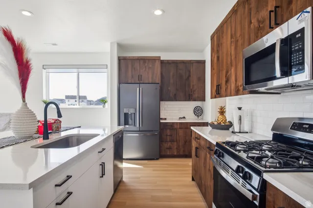 Kitchen with stainless steel appliances, light stone counters, light wood finished floors, recessed lighting, and dark wood finish cabinetry