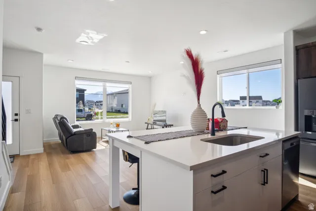 Kitchen with light wood finished floors, open floor plan, stainless steel fridge with ice dispenser, a center island with sink, and plenty of natural light