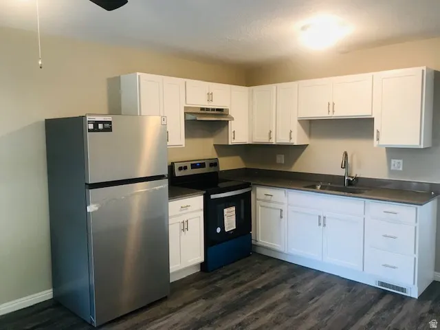 Kitchen with stainless steel appliances, dark countertops, white cabinetry, and dark wood-style flooring