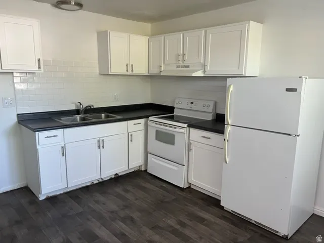 Kitchen with white appliances, dark countertops, and white cabinetry