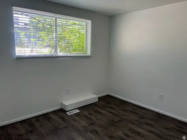 Empty room featuring baseboards and dark wood-type flooring