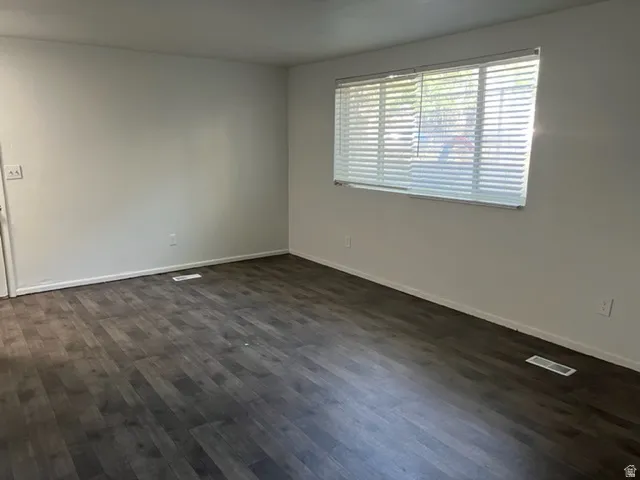Spare room featuring dark wood-style flooring and baseboards