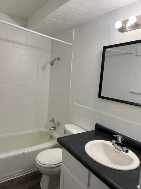 Bathroom with vanity, bathing tub / shower combination, tile walls, a wainscoted wall, and dark wood-style floors