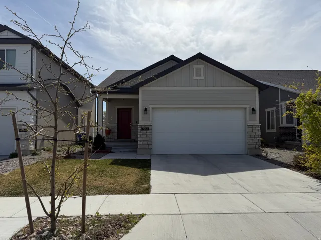 Craftsman-style home featuring board and batten siding, stone siding, a garage, driveway, and a front lawn
