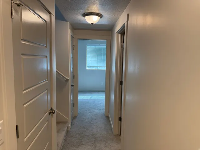Hall featuring a textured ceiling and light colored carpet