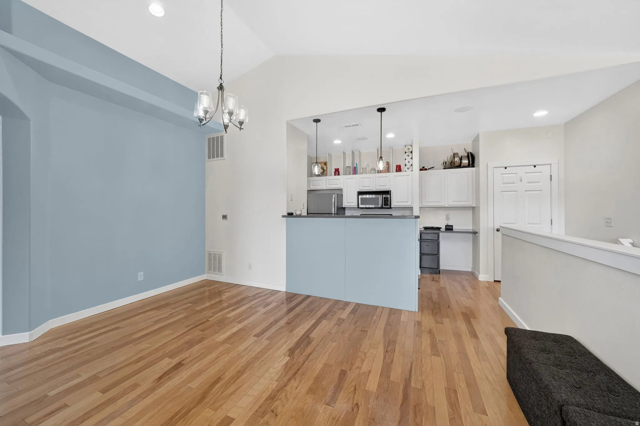 Kitchen with dark countertops, open floor plan, white cabinets, stainless steel appliances, and light wood-style flooring