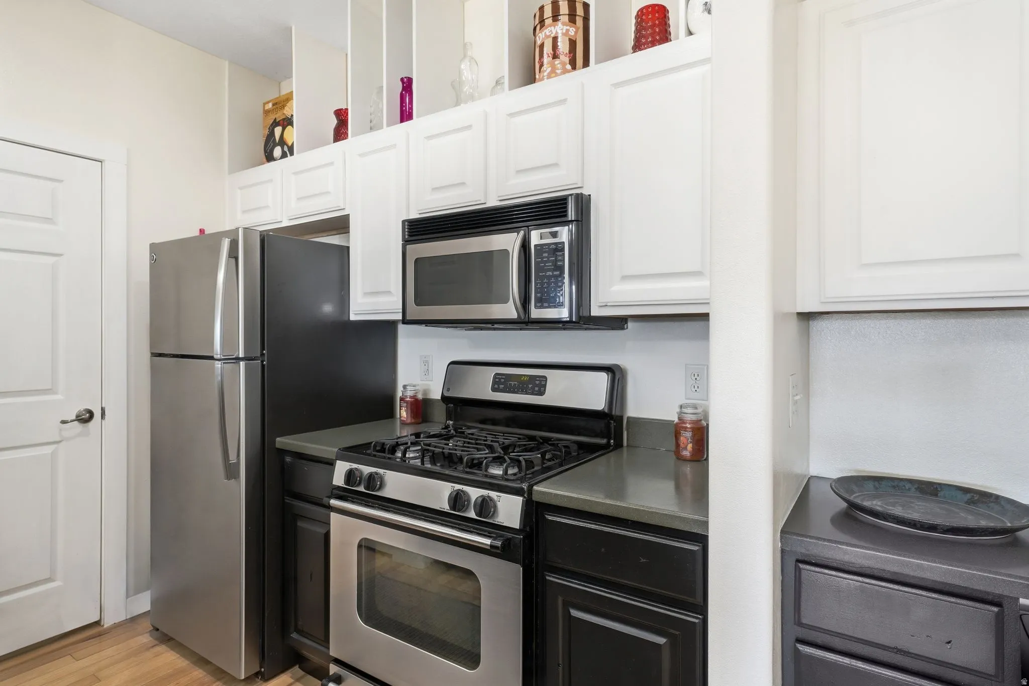 Dual tone kitchen featuring stainless steel appliances, two tone color scheme, light wood finished floors, and dark countertops