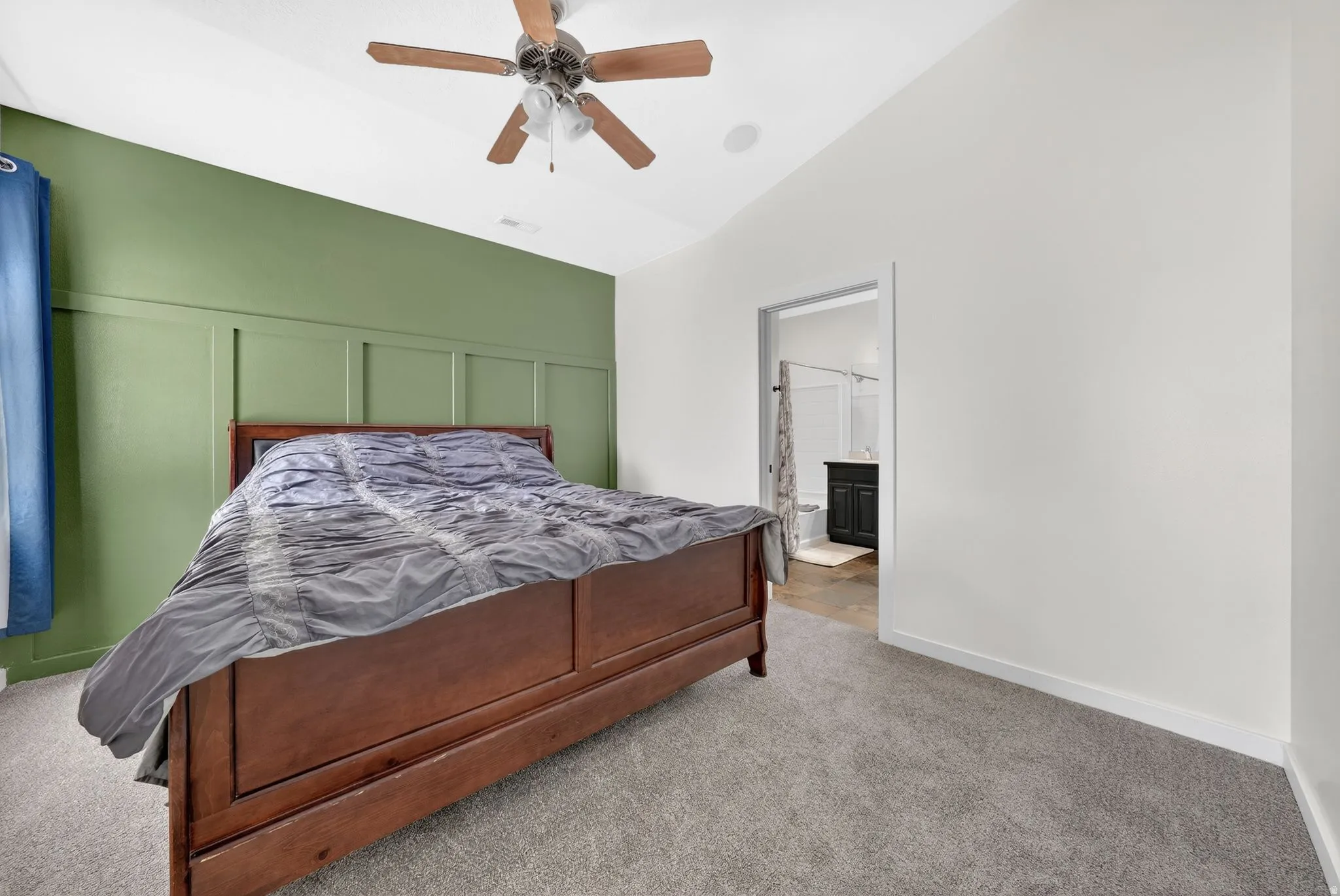 Carpeted bedroom with lofted ceiling, ceiling fan, a decorative wall, and ensuite bathroom