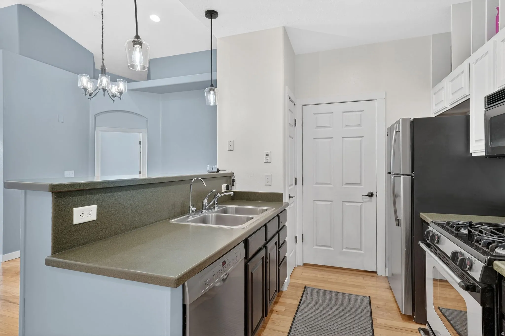 Kitchen featuring stainless steel appliances, light wood-style floors, a peninsula, suspended lighting, and white cabinets