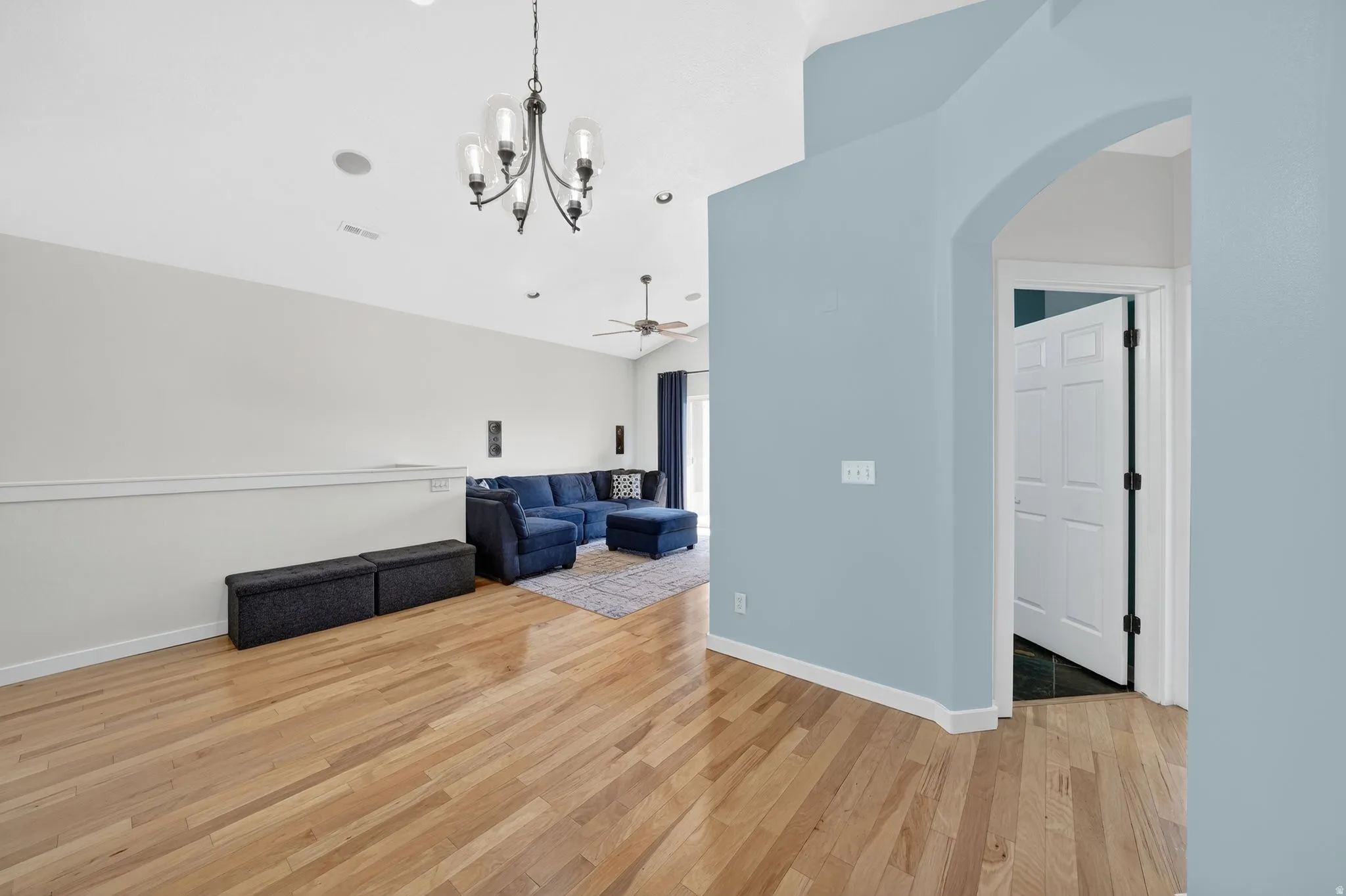 Unfurnished living room with arched walkways, light wood-type flooring, suspended lighting, a ceiling fan, and vaulted ceiling