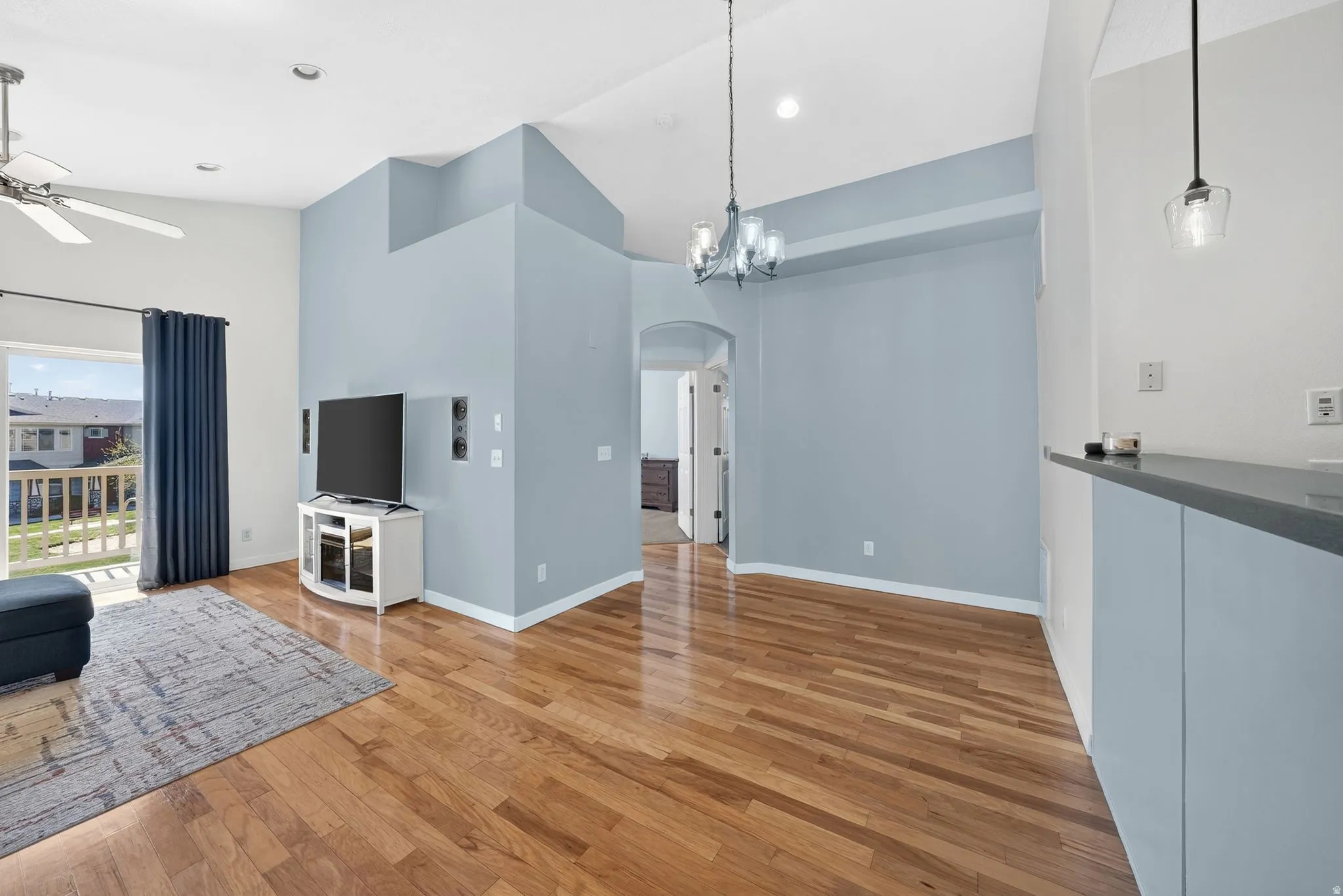 Unfurnished living room featuring arched walkways, light wood-type flooring, a ceiling fan, a chandelier, and vaulted ceiling