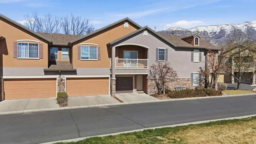 View of front facade featuring a garage, stucco siding, a balcony, and stone siding
