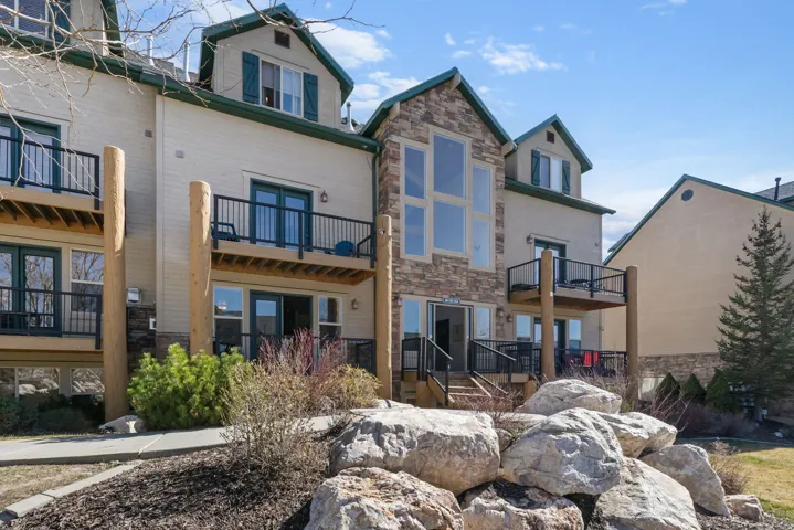 Back of house with stone siding and a balcony