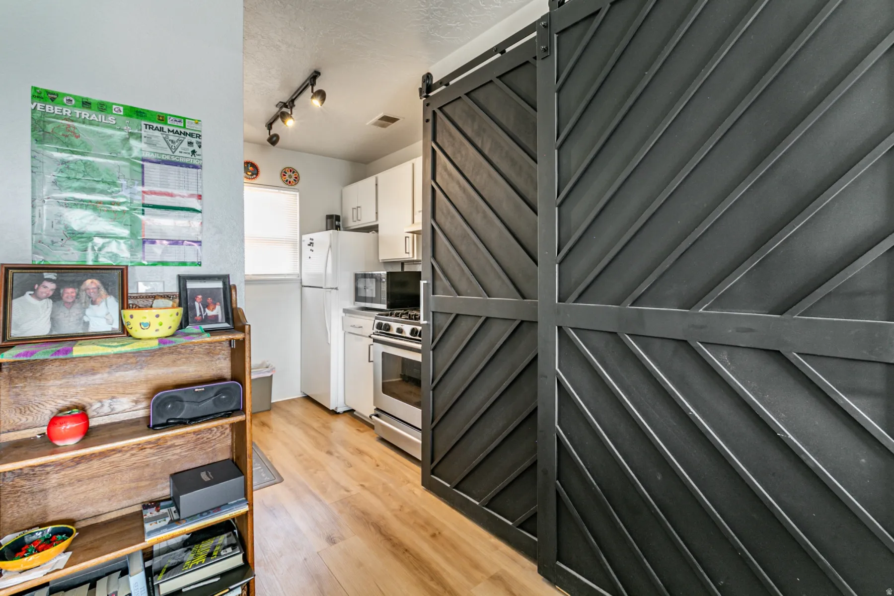 Kitchen featuring a barn door, white cabinets, a textured ceiling, stainless steel appliances, and light wood-type flooring
