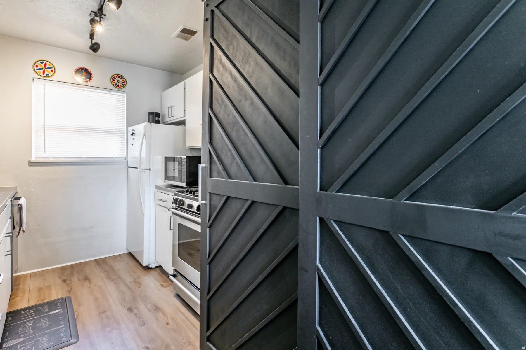 Kitchen featuring white cabinets, stainless steel appliances, light wood-type flooring, light countertops, and rail lighting