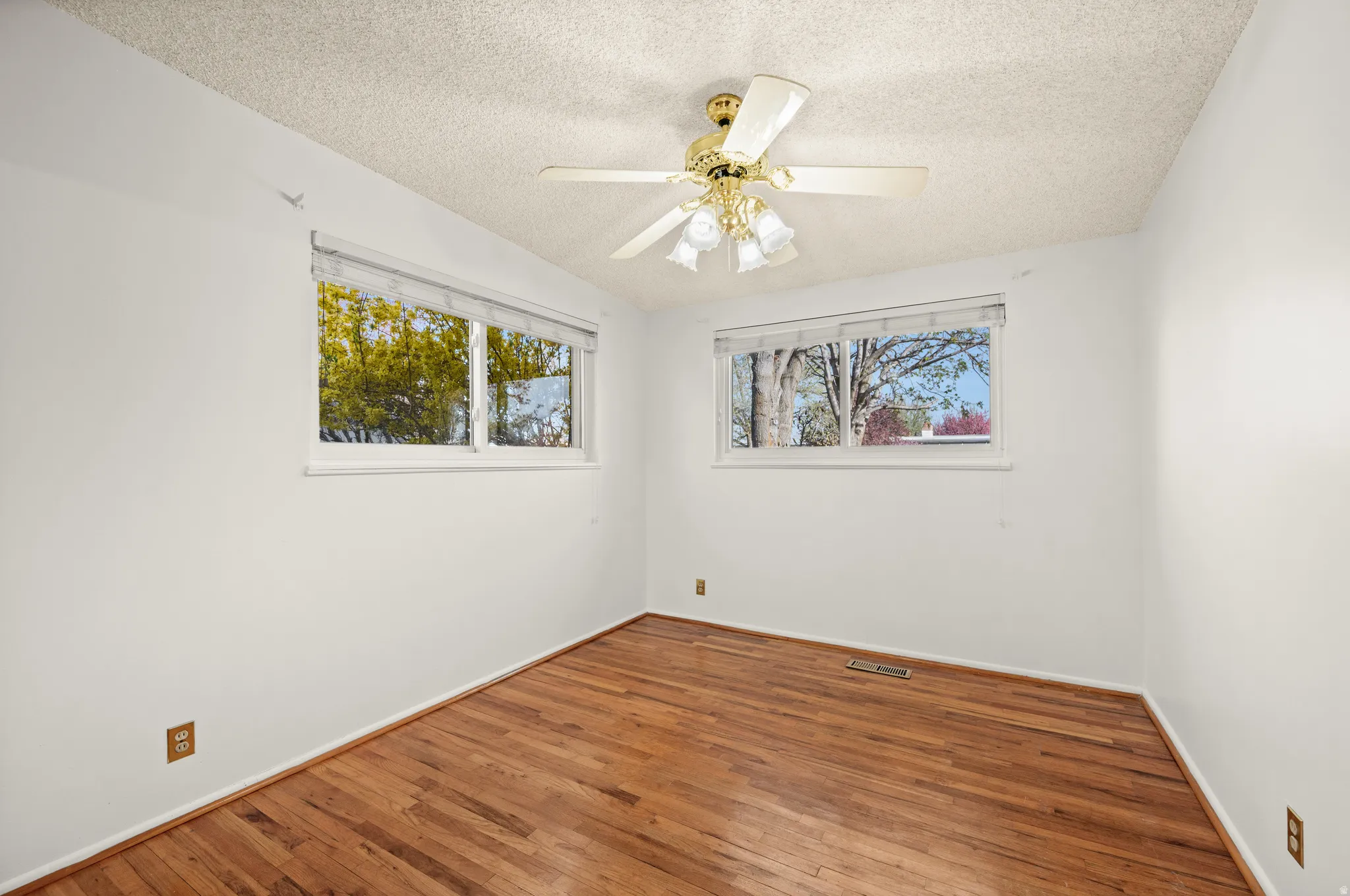 Empty room featuring wood finished floors, ceiling fan, a textured ceiling, and plenty of natural light