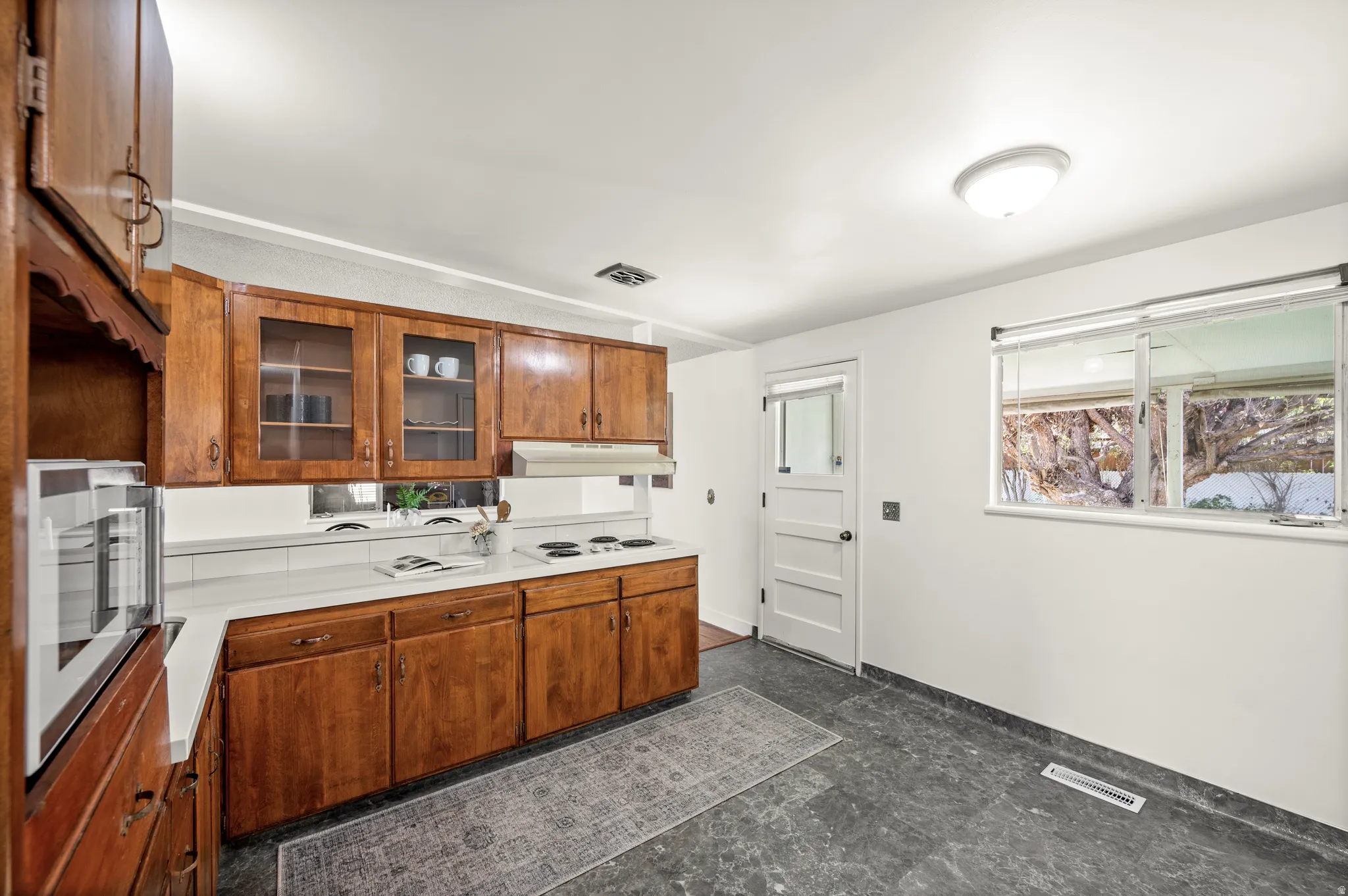 Kitchen featuring wood finish cabinetry, light countertops, glass insert cabinets, and white electric cooktop