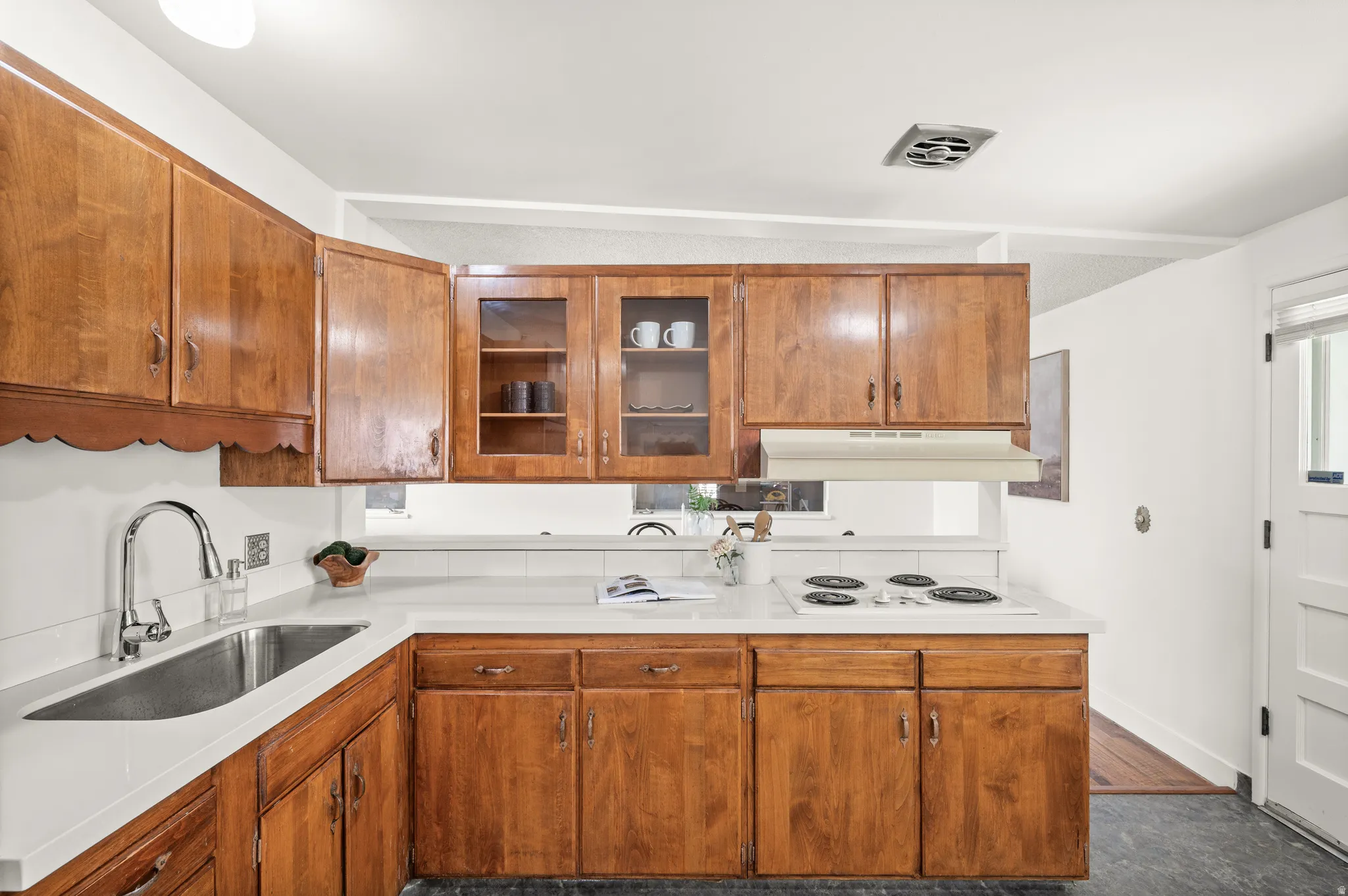Kitchen with light countertops, wood finish cabinets, white electric stovetop, and glass insert cabinets