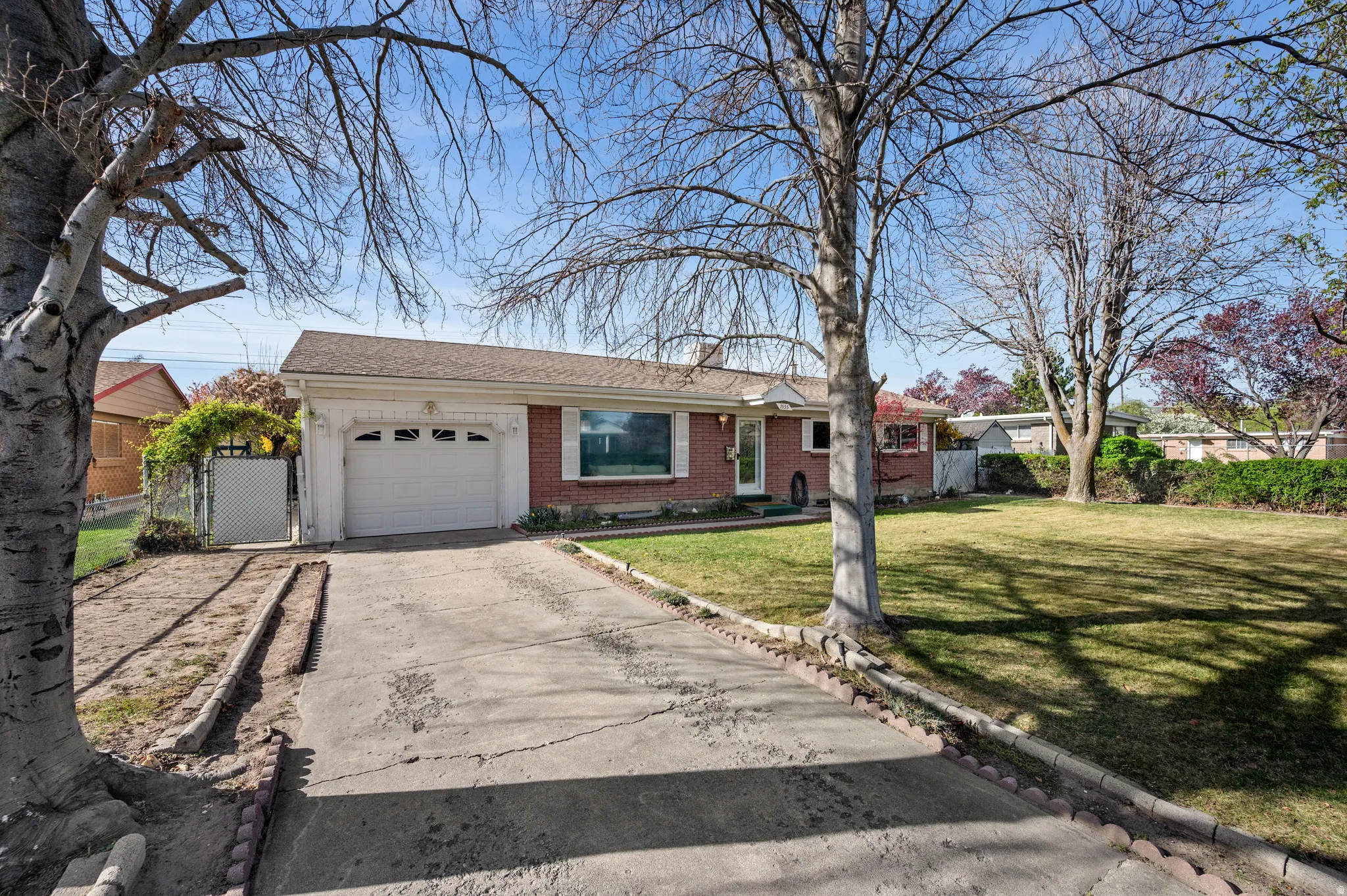 Ranch-style home with an attached garage, concrete driveway, brick siding, a gate, and a shingled roof