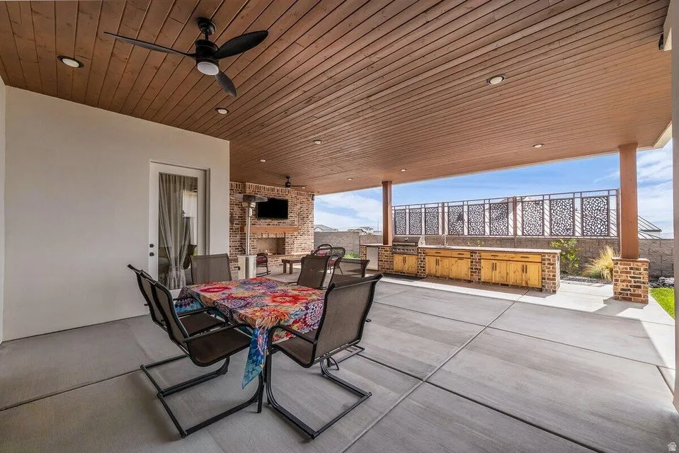 View of patio featuring an outdoor kitchen / dining area, ceiling fan, and an outdoor brick fireplace